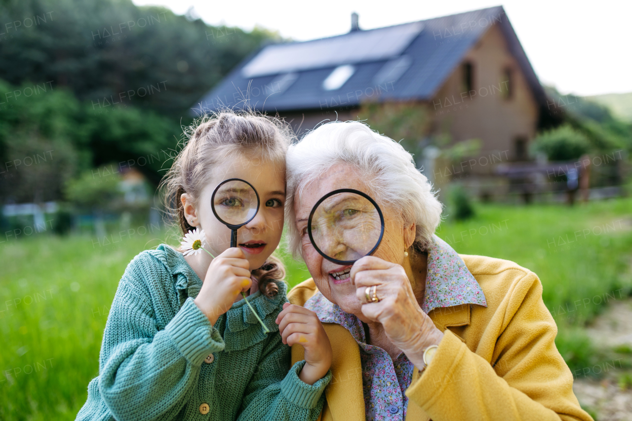 Granddaughter exploring wildlife with elderly grandma, using magnifying glass to look at insect. Senior lady spending time with young girl, enjoying together time. Weekend in cottage.