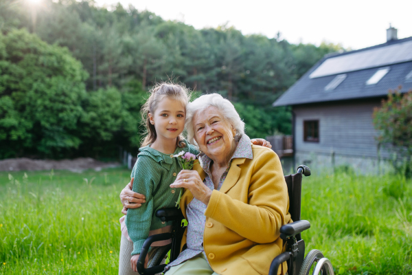 Granddaughter spending time with elderly grandma, picking widlflowers. Senior lady in wheelchair spending time in nature. Weekend in cottage.