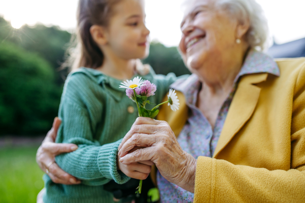 Granddaughter spending time with elderly grandma, picking wildflowers. Senior lady spending time in nature. Weekend in cottage.