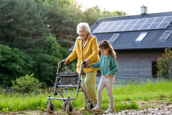 Granddaughter spending time with elderly grandma, companionship. Senior lady with walker spending time in nature. Weekend in cottage.