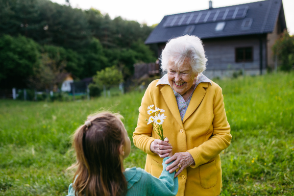 Granddaughter spending time with elderly grandma, picking wildflowers. Senior lady spending time in nature. Weekend in cottage.