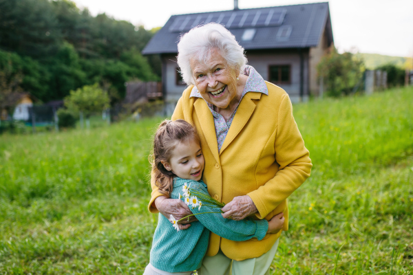 Granddaughter spending time with elderly grandma, picking wildflowers. Senior lady spending time in nature. Weekend in cottage.