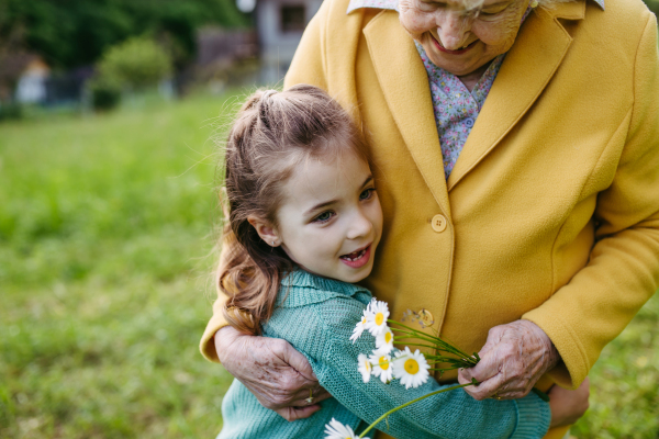 Granddaughter spending time with elderly grandma, picking wildflowers. Senior lady spending time in nature. Weekend in cottage.