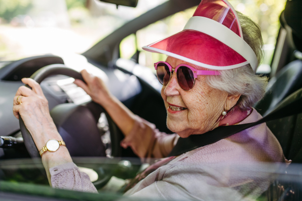 Happy senior woman driving car alone, enjoying the car ride. Safe driving for elderly adults, older driver safety. Driving license renewal at older age.