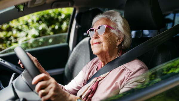 Happy senior woman driving car alone, enjoying the car ride. Safe driving for elderly adults, older driver safety. Driving license renewal at older age.