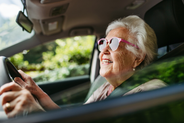 Happy senior woman driving car alone, enjoying the car ride. Safe driving for elderly adults, older driver safety. Driving license renewal at older age.