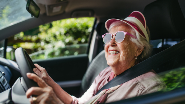 Happy senior woman driving car alone, enjoying the car ride. Safe driving for elderly adults, older driver safety. Driving license renewal at older age.