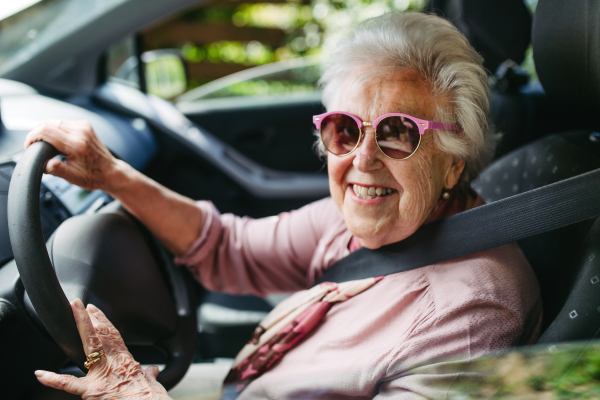 Cool senior woman in sunglasses driving car alone, enjoying the car ride. Safe driving for elderly adults, older driver safety. Driving license renewal at older age.