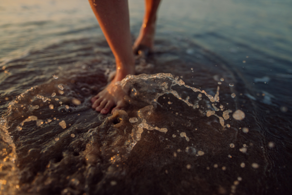 Woman walking on the beach during sunset, close-up of feet.