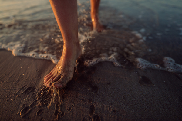 Woman walking on the beach during sunset, close-up of feet.