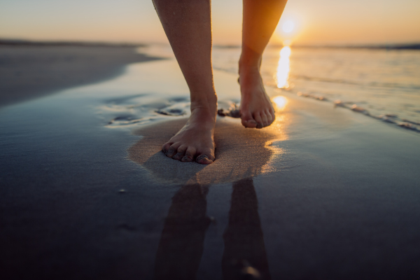 Woman walking on the beach during sunset, close-up of feet.