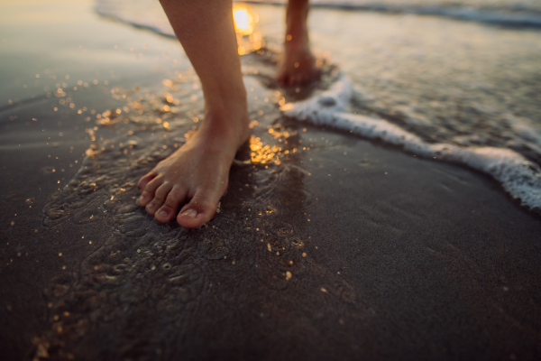 Woman walking on the beach during sunset, close-up of feet.