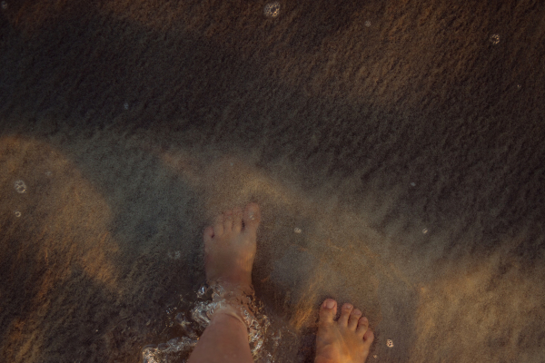 Woman walking on the beach during sunset, close-up of feet.