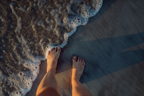 Woman walking on the beach during sunset, close-up of feet.