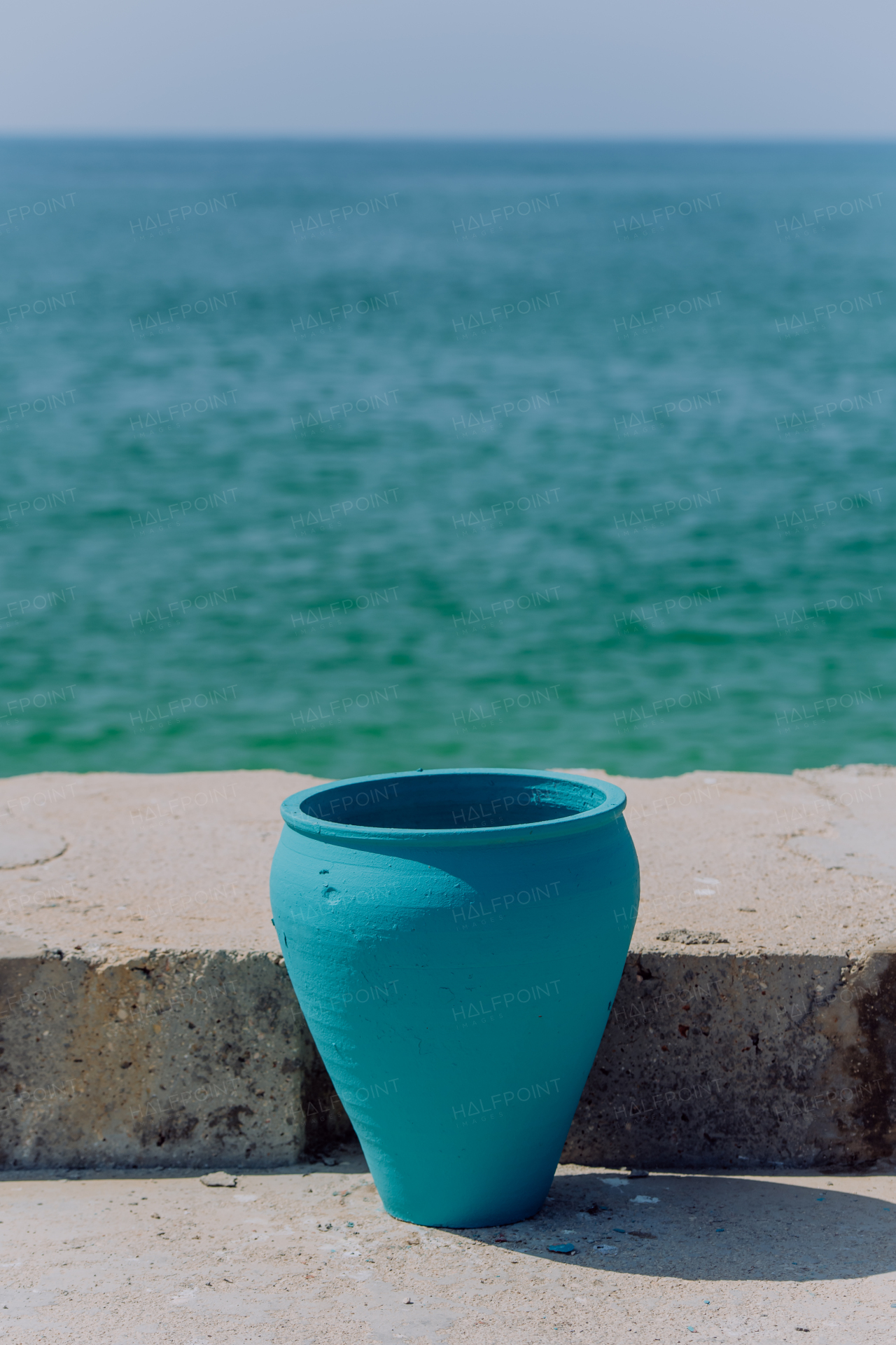 Close up of blue amphora with ocean in the background.