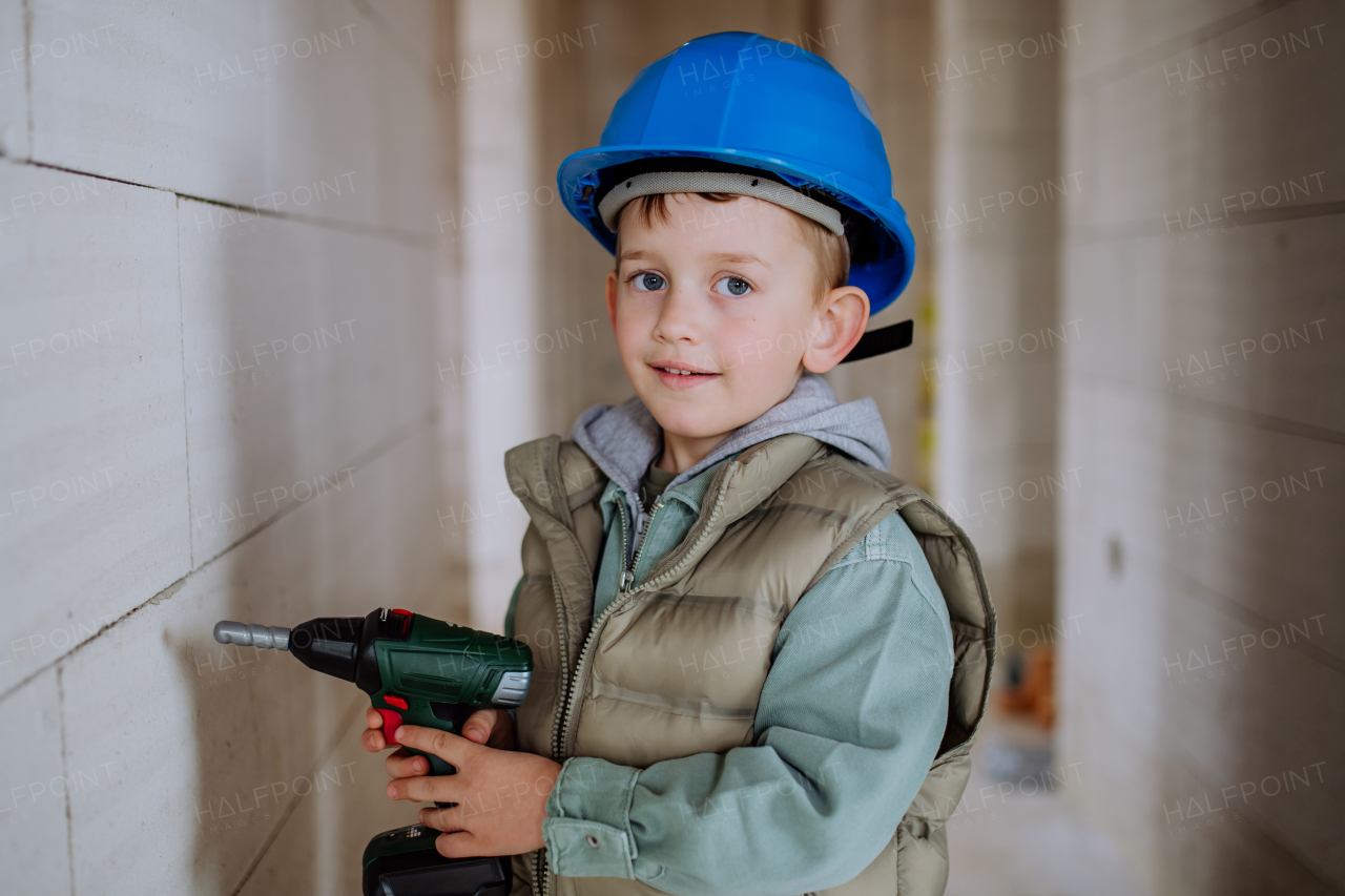 Portrait of a little boy in unfinished house posing with helmet and drill.