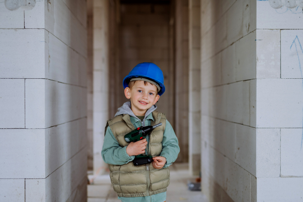 Portrait of a little boy in unfinished house posing with helmet and drill.