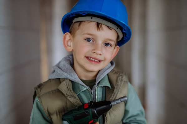 Portrait of a little boy in unfinished house posing with helmet and drill.