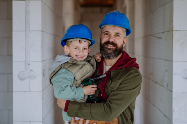 Portrait of father and his little son in their unfinished house with helmet and tools.