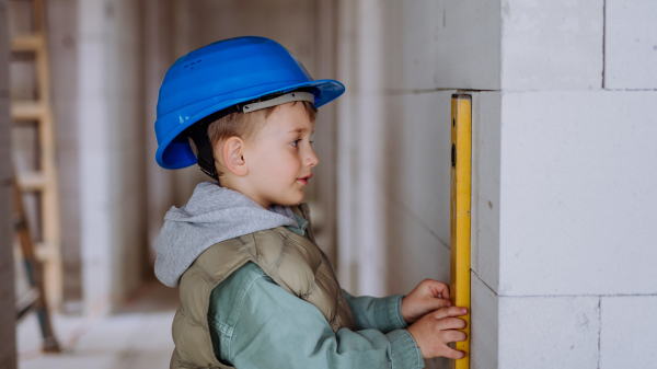 Little boy in unfinished house measuring wall in unfinished house with a spirit level.