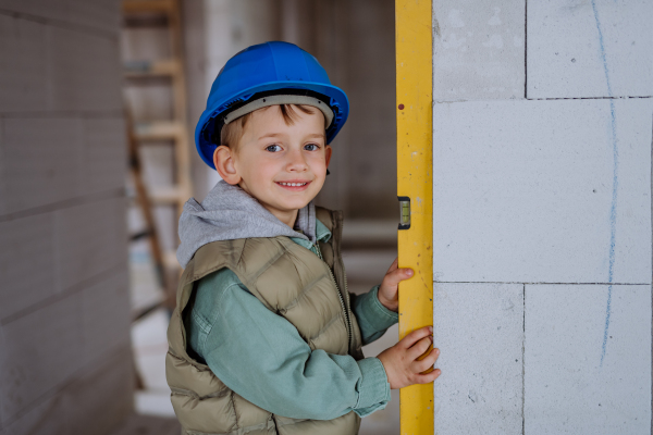 Little boy in unfinished house measuring wall in unfinished house with a spirit level.