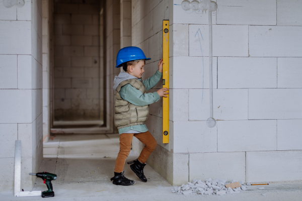 Little boy in unfinished house measuring wall in unfinished house with a spirit level.