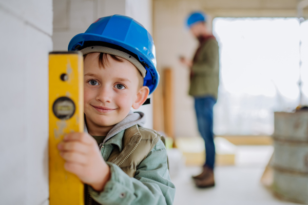 Little boy in unfinished house measuring wall in unfinished house with a spirit level.