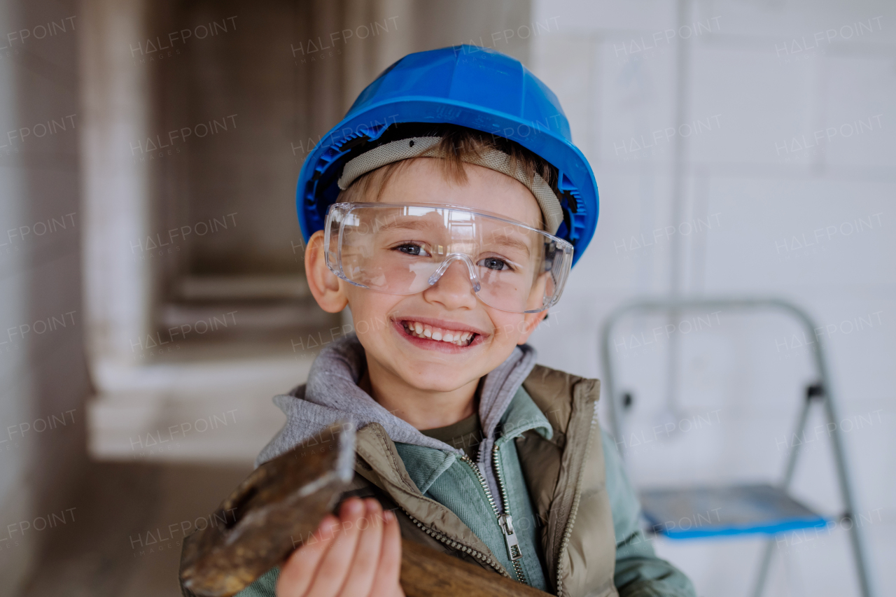 Portrait of a little boy in unfinished house posing with helmet and drill.