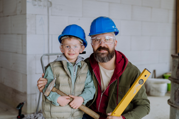 Portrait of father and his little son in their unfinished house with helmet and tools.