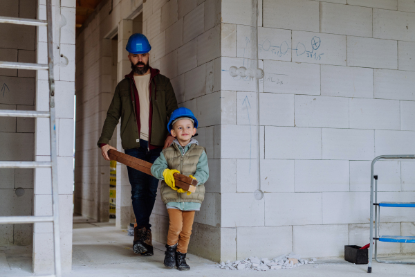 Father and his little son working in their unfinished house, carring a wooden panicle.