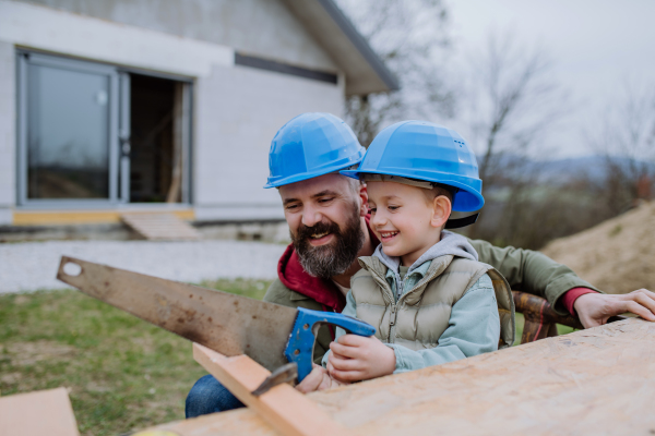 Father and his little son working together in front of their unfinished house.