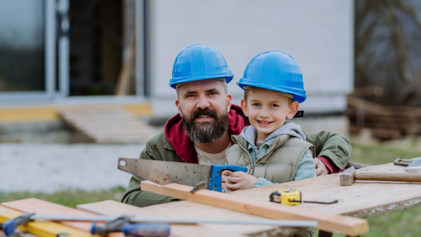 Father and his little son working together in front of their unfinished house.