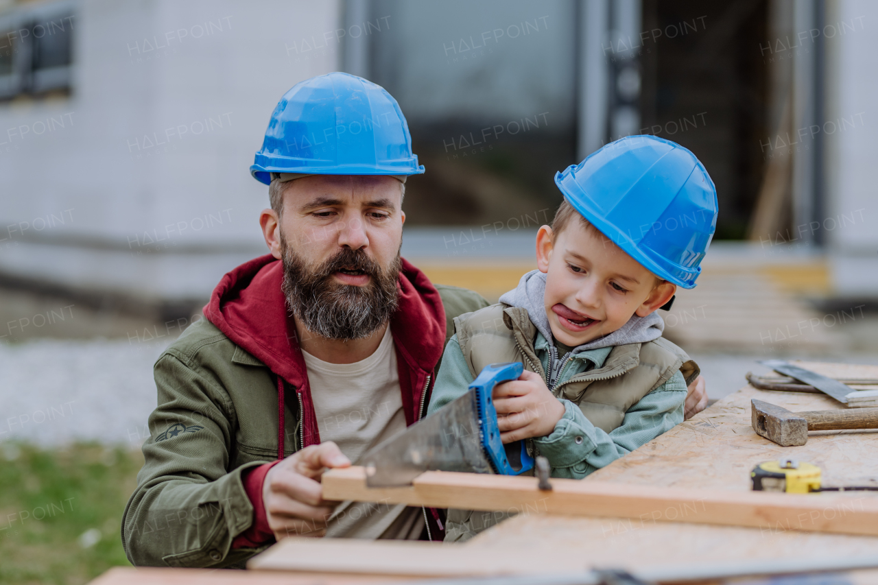 Father and his little son working together in front of their unfinished house.