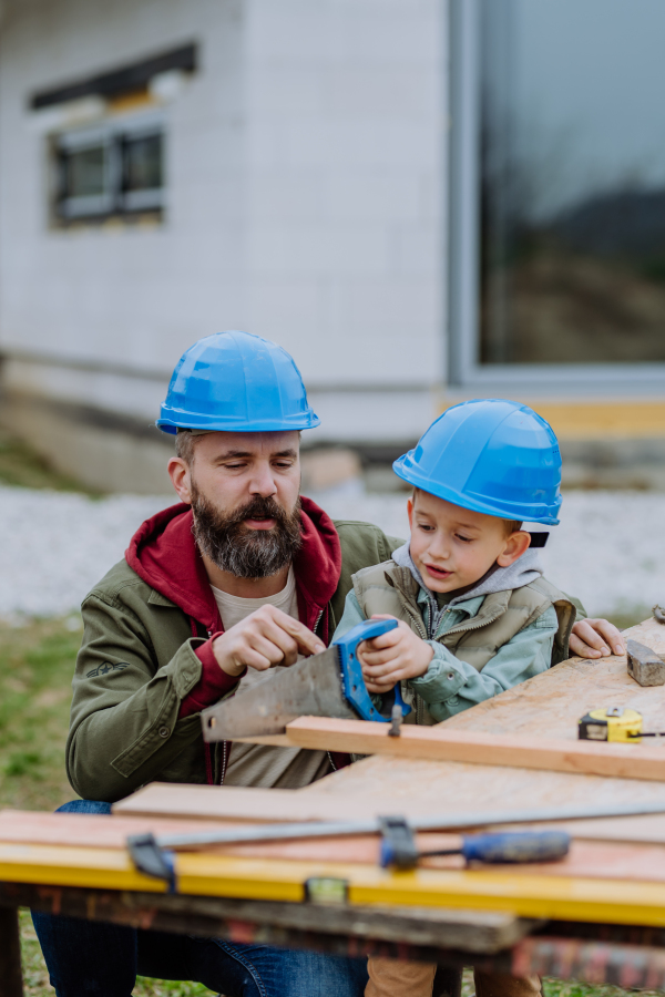 Father and his little son working together in front of their unfinished house.