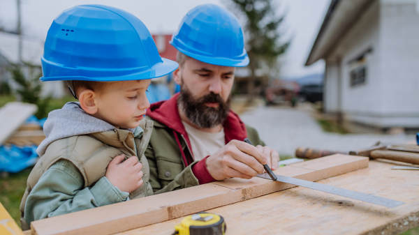 Father and his little son working together in front of their unfinished house.