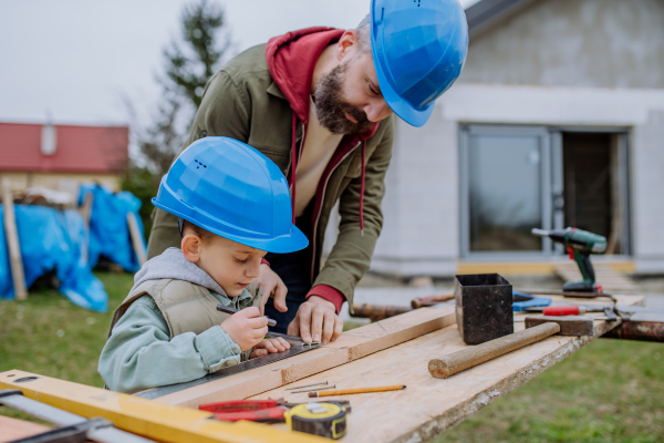 Father and his little son working together in front of their unfinished house.