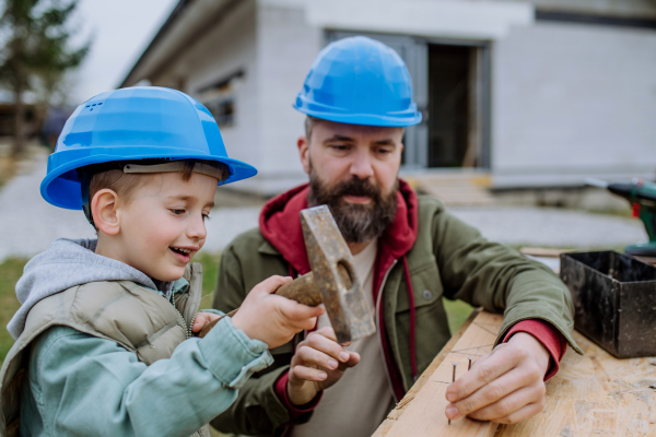 Father and his little son working together in front of their unfinished house.