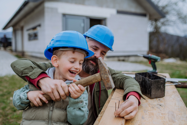 Father and his little son working together in front of their unfinished house.