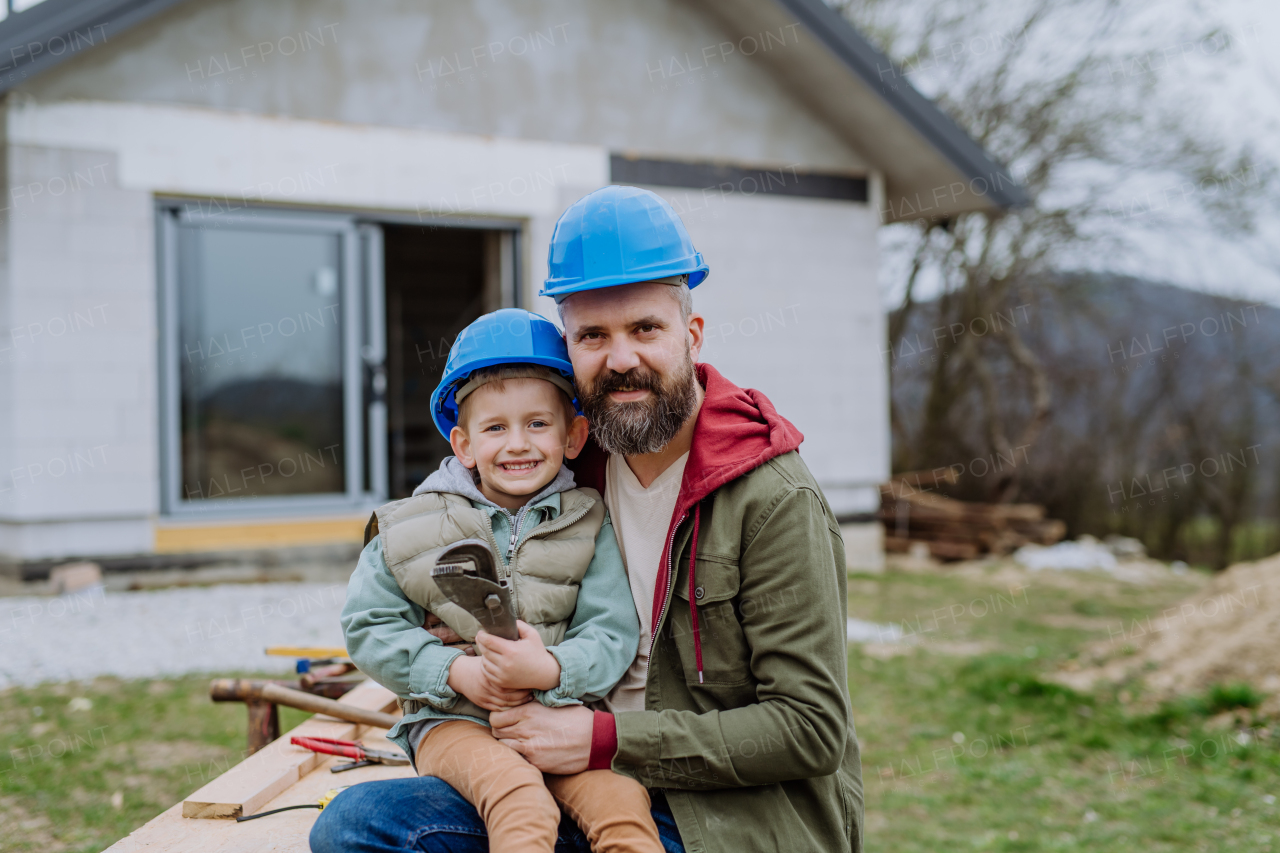 Portrait of father with his little son in front of their new unfinished house.