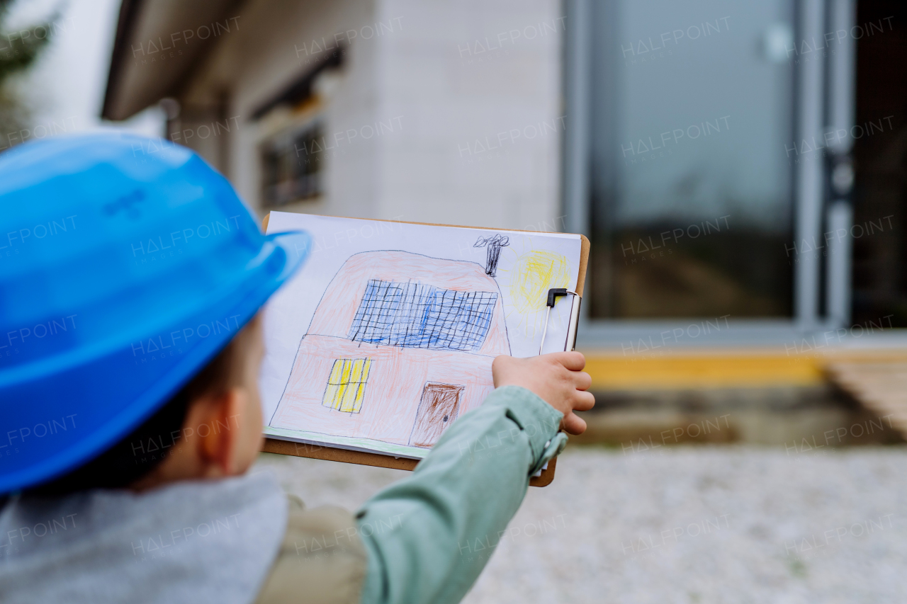 LIttle boy with drawn picture in front of their new unfinished house.