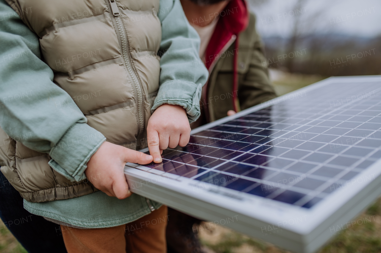 Close-up of father and his little son holding solar panel, in front of their unfinished house.