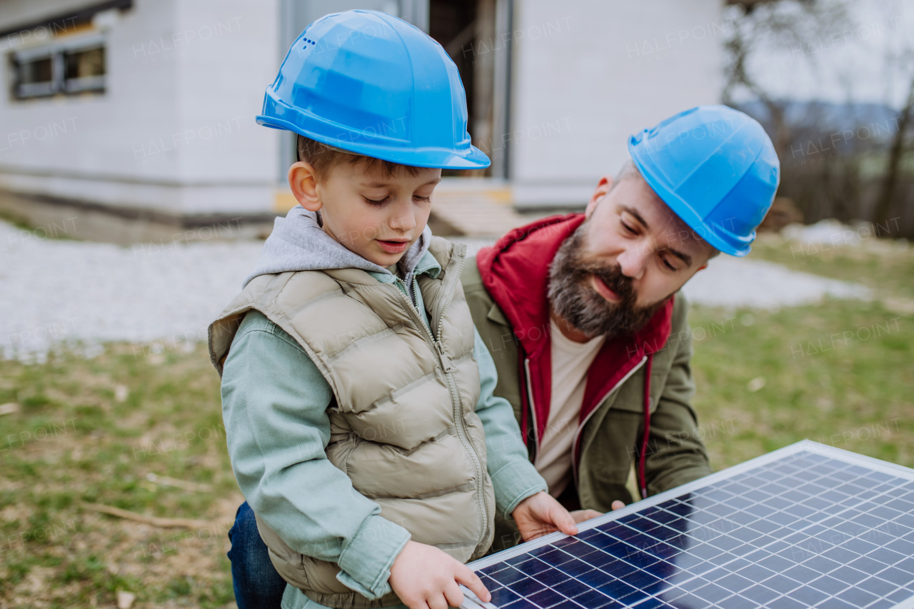 Close-up of father and his little son holding solar panel, in front of their unfinished house.