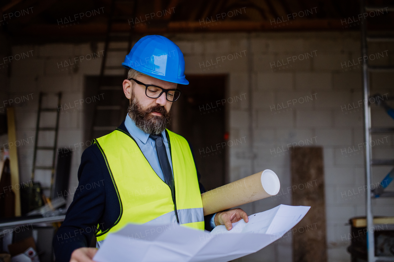 Mature businessman controlling blueprints from an unfinished house.