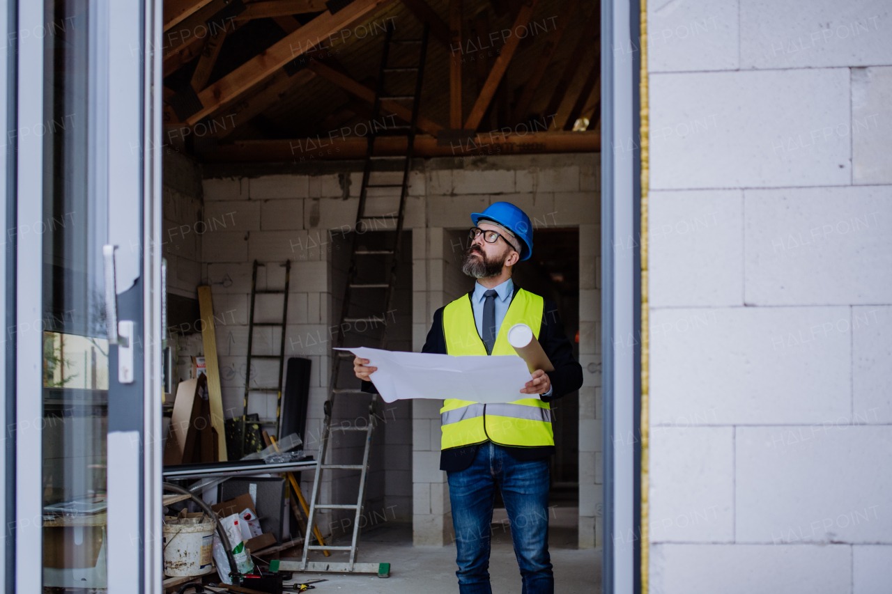 Mature businessman controlling blueprints from an unfinished house.