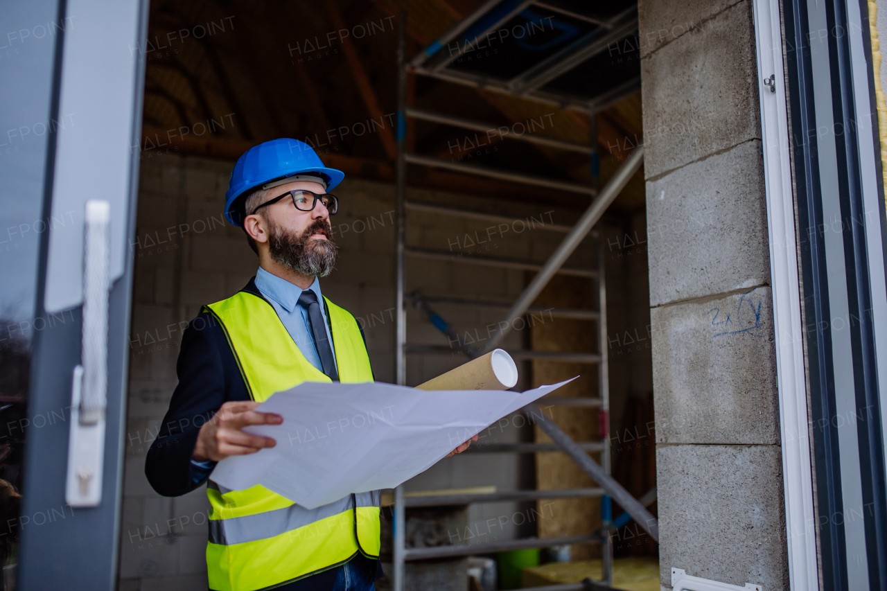 Mature businessman controlling blueprints from an unfinished house.