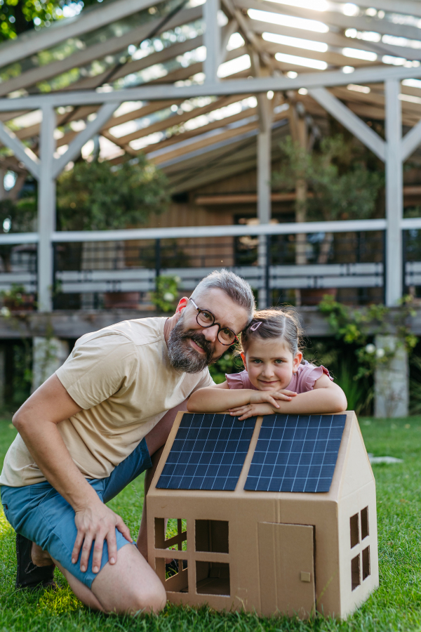 Dad and girl playing with house with solar panels on roof, learning about solar energy. Rooftop solar or photovoltaic system. Sustainable future for next generation concept.