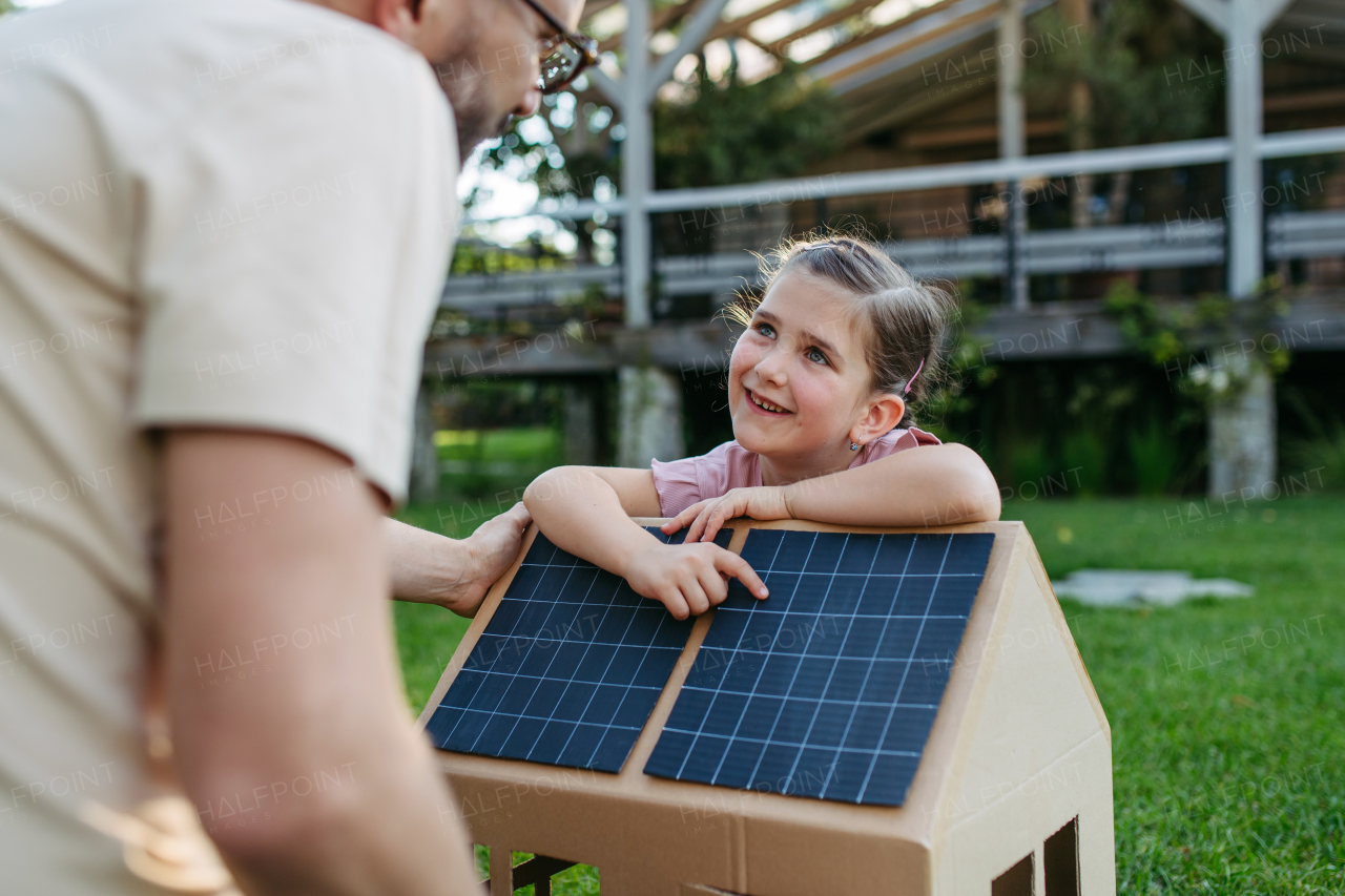 Dad and girl playing with house with solar panels on roof, learning about solar energy. Rooftop solar or photovoltaic system. Sustainable future for next generation concept.