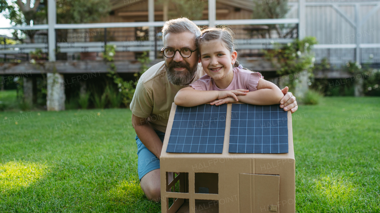 Dad and girl playing with house with solar panels on roof, learning about solar energy. Rooftop solar or photovoltaic system. Sustainable future for next generation concept.