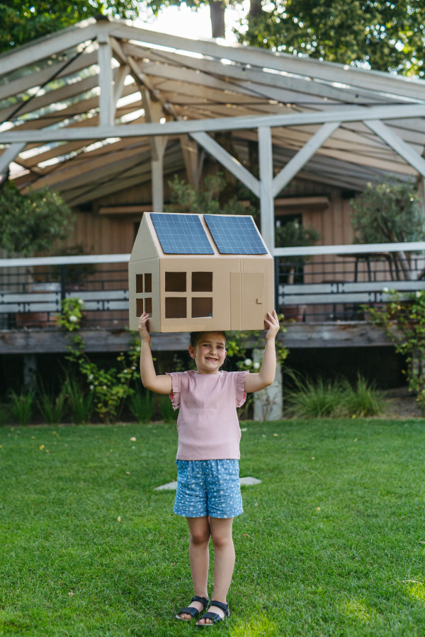 Girl playing with house with solar panels on roof, learning about solar energy. Rooftop solar or photovoltaic system. Sustainable future for next generation concept.