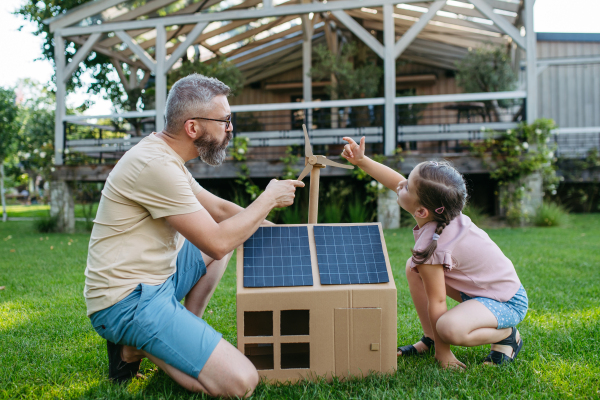 Dad and girl playing with house with solar panels on roof, learning about solar energy. Rooftop solar or photovoltaic system. Sustainable future for next generation concept.